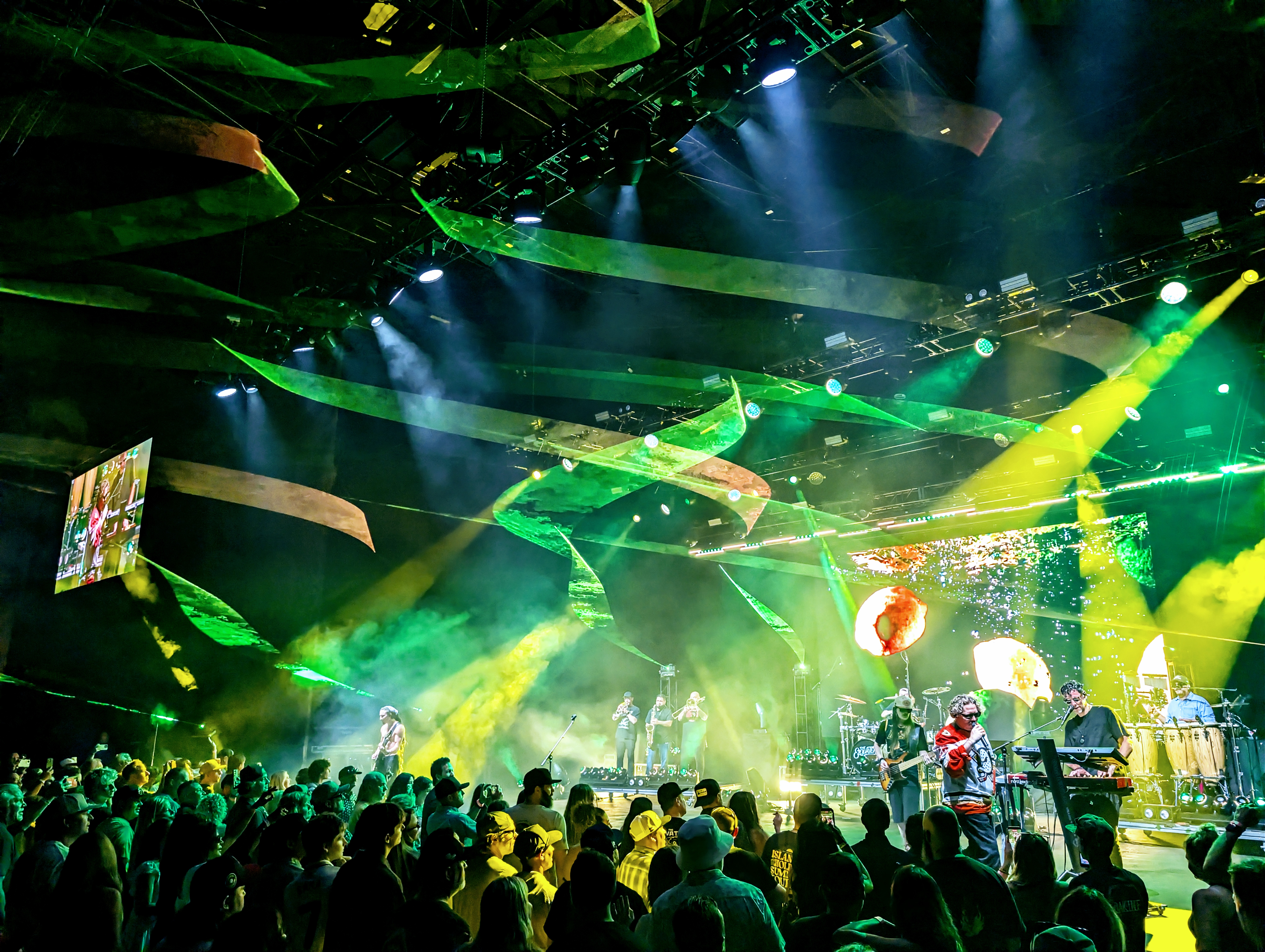 The Elovaters performing beneath green and yellow lights at Pacific Amphitheatre