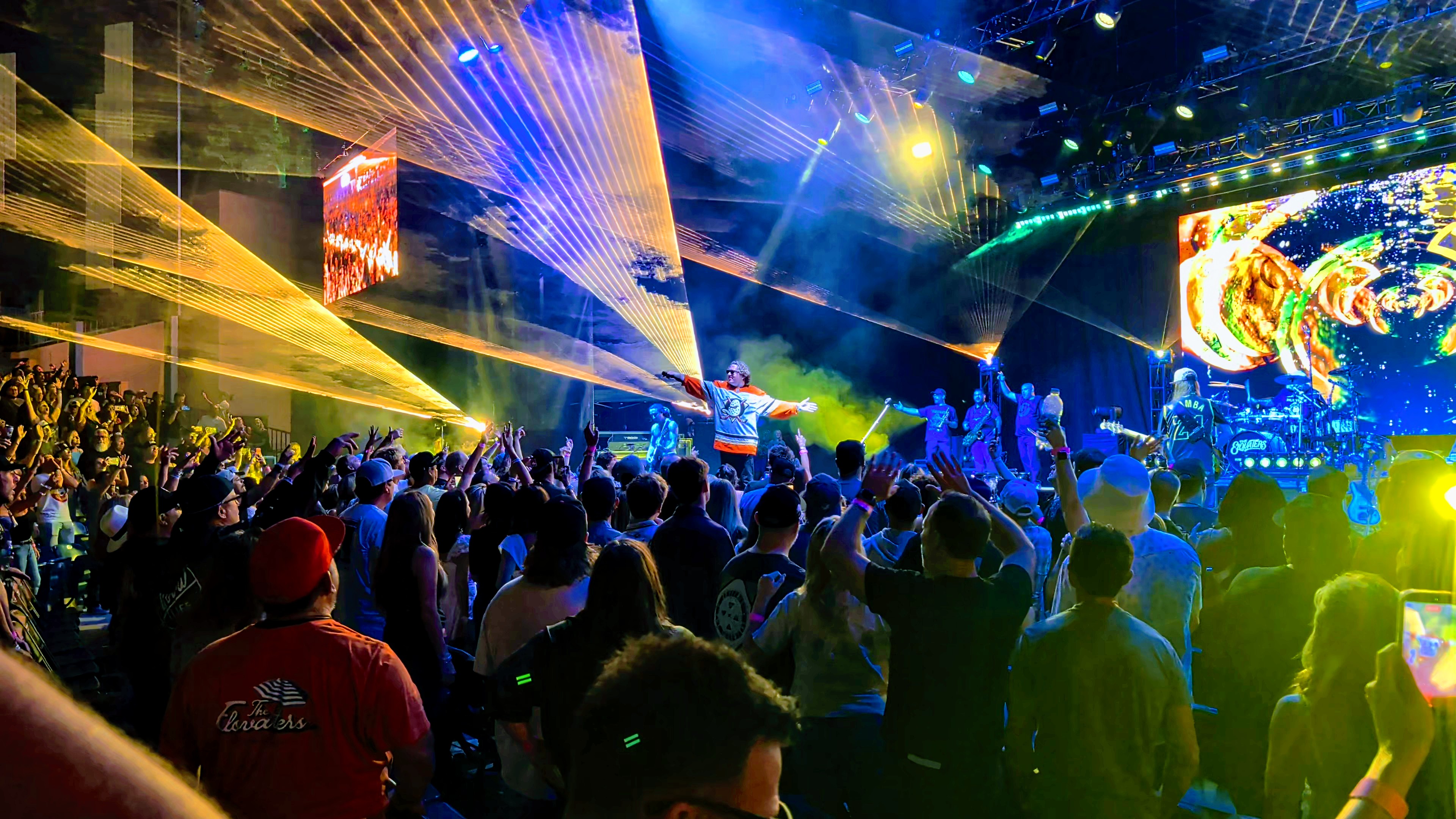 The Elovaters performing beneath yellow and blue lasers at Pacific Amphitheatre